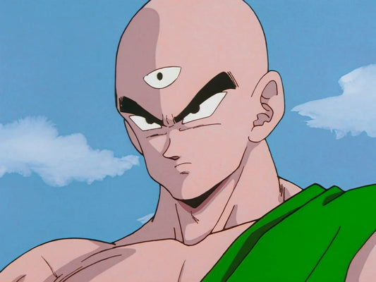 Ten Shin Han en gros plan, crâne rasé et troisième œil au milieu du front, sourcils froncés, une étoffe verte sur l'épaule, devant un ciel bleu nuageux.
